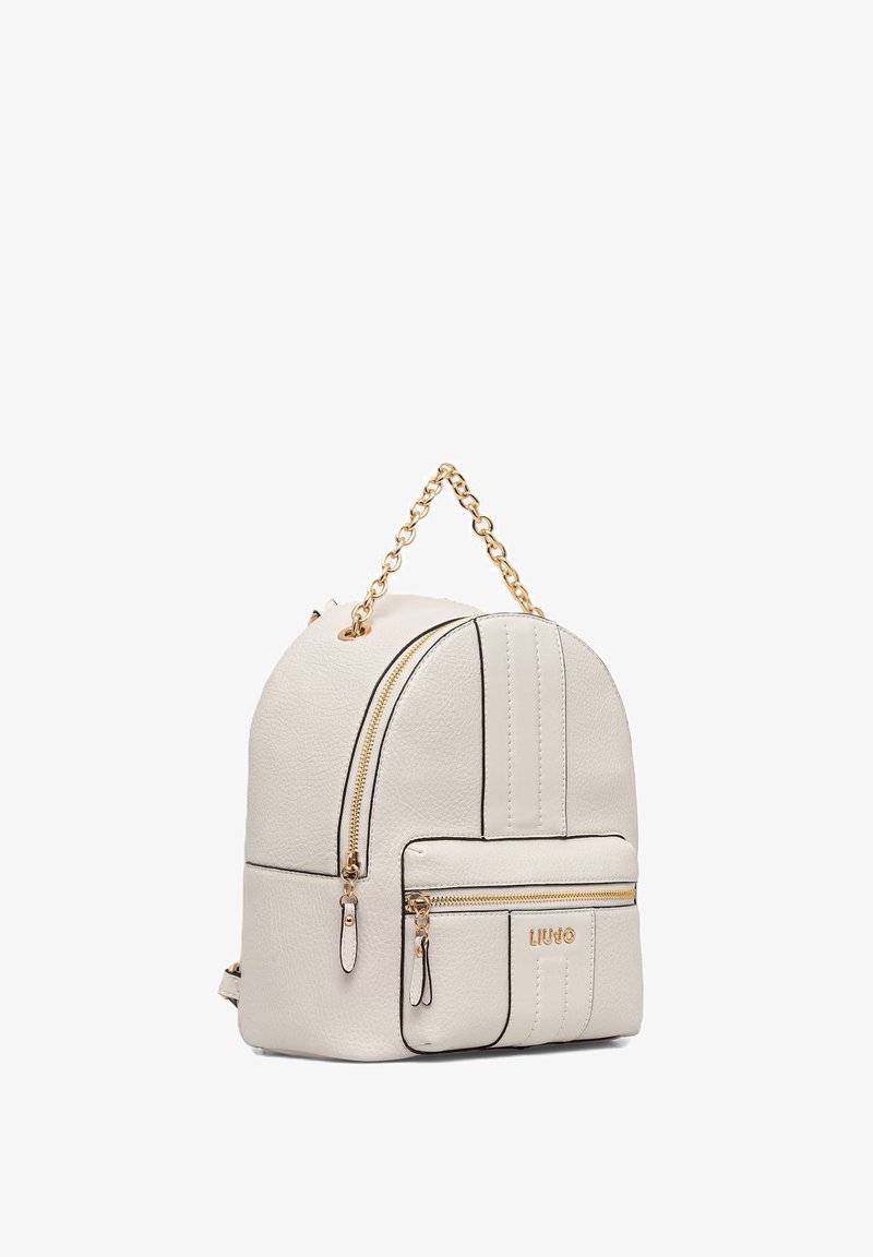 Pequeña mochila de cuero color crema con bolsillo delantero con cremallera, asa de cadena dorada y detalles de cremallera dorados.