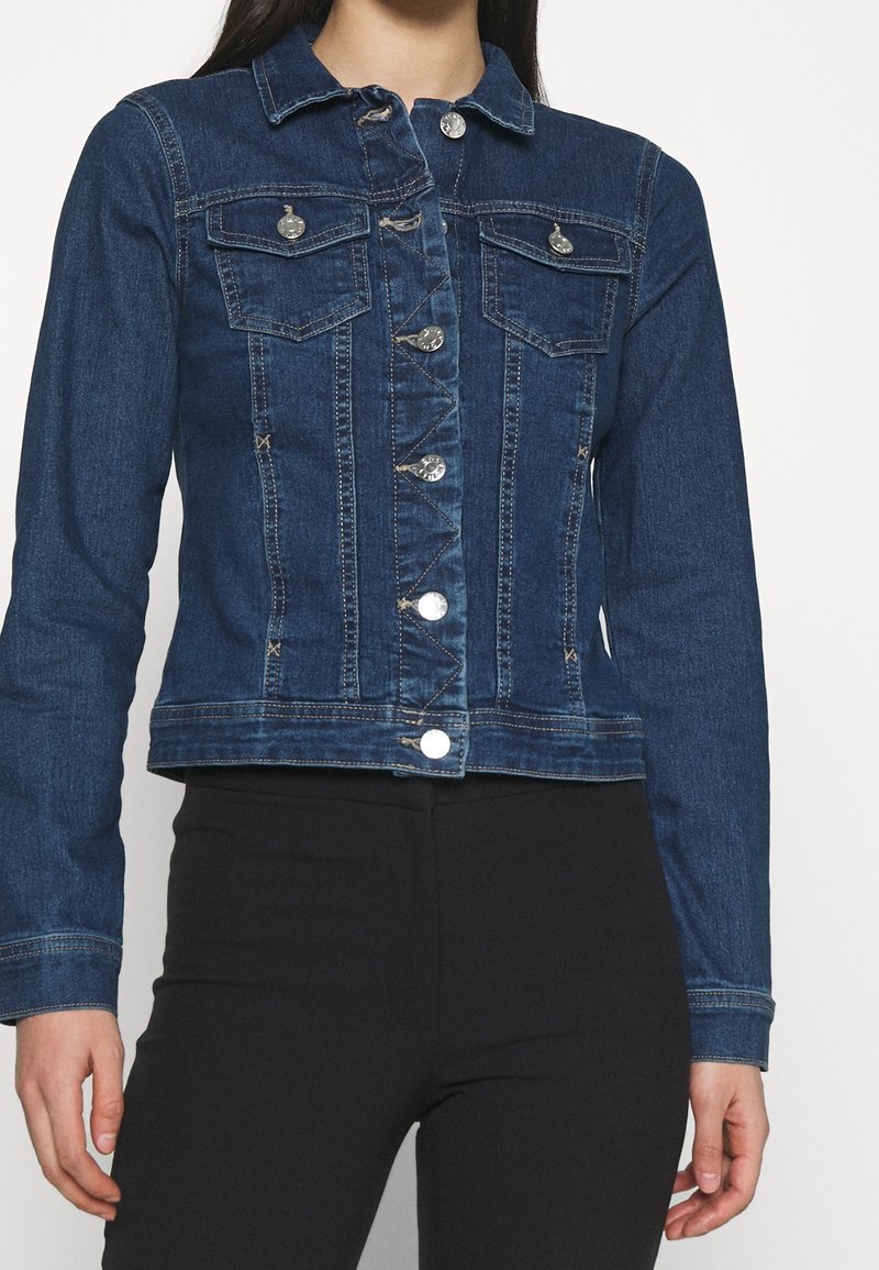 Mörkblå denimjacka med långa ärmar, två bröstfickor och silverfärgade knappar. Strukturerad tyg och kort design.