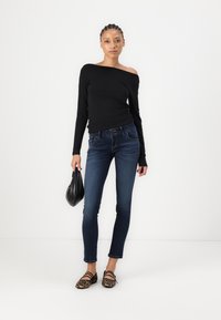Top lungo nero off-the-shoulder a maniche lunghe, jeans skinny blu, borsa nera e ballerine marroni con stampa leopardo e cinturini neri. Design semplice.