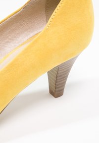 Żółte zamszowe buty na wysokim obcasie z fakturowanym drewnianym obcasem i gładkim wykończeniem wnętrza. Okrągły nos i subtelne detale przeszyć widoczne.