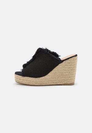 Black open-toe wedge sandal with frayed fabric upper and woven natural fiber platform heel on a white background.