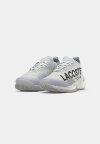 LACOSTE sportcipő fehér és szürke színben, sima felső anyaggal, kiemelkedő logónyomattal és mintás talpú gumitalppal.