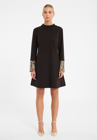 Schwarzes Kleid mit langen Ärmeln, das gemusterte Manschetten in Gold- und Blautönen aufweist. Das Design ist A-Linie mit einem Stehkragen.