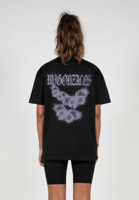 Sort t-shirt med korte ærmer, der har et grafisk motiv af en lilla sommerfugl og tekst på ryggen. Lavet af bomuld, med en løs og afslappet pasform.