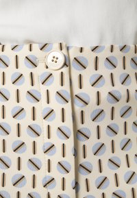 Mønstrede bukser med en cremefarvet bund, blå cirkler og brune striber. Livstykket har en hvid knap og stikninger.