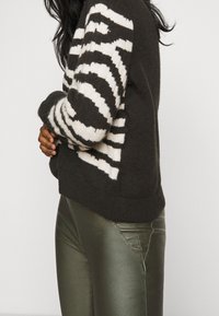 Leggings metálicos verde oscuro combinados con un suéter de rayas en blanco y negro, que cuenta con una textura suave y un ajuste acogedor.
