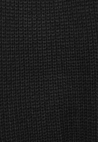 Μαύρο πλεκτό ύφασμα με υφή και χοντρή βελονιά. Το υλικό φαίνεται μαλακό και πυκνό, κατάλληλο για ζεστασιά και άνεση.