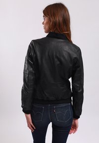 Schwarze Lederbomberjacke mit geripptem Kragen und Bündchen, die über eine glatte Textur und eine taillierte Silhouette verfügt.