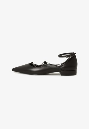 Chaussure plate en cuir noir avec un bout pointu, une bride à la cheville et un détail de chaîne décoratif. Dispose d'un petit talon carré et d'une texture lisse.