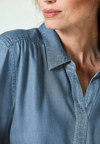 Hellblaue Denimbluse mit einem Kragen, weichem Material, gerafftem Schulterdetail und einer lockeren Passform.