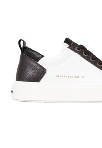 Sneaker bianco in pelle con accenti testurizzati marroni, marchiatura dorata, linguetta sul tallone nera e suola spessa bianca. Occhielli con lacci marroni.