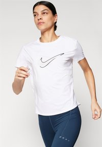 Hvit atletisk t-skjorte med svart swoosh-logo, korte ermer og avslappet passform, sammen med mørkeblå leggings med aksentdetaljer.