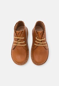 Chaussures en cuir marron avec des bords festonnés, dotées de lacets beiges, d'un bout rond et d'une couture contrastante. Texture lisse et design classique.