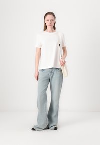 Hvid kortærmet t-shirt med subtilt logo, parret med lyseblå flared jeans og en lille hvid skuldertaske. Sorte sko.