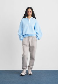 Svetlomodrý sveter s bielym golierom, šedé tepláky a svetlé tenisky. Na svetriku sa nachádza logo.