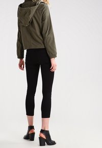 Kort olijfgroen jack met capuchon, gecombineerd met zwarte skinny jeans en open teen schoenen met blokhak. Eenvoudig ontwerp, zonder patronen.