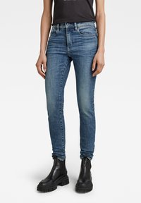 Jeans de denim azules ajustados con un acabado ligeramente descolorido, diseño de cinco bolsillos y cierre de botón, combinados con botas negras hasta el tobillo.