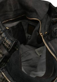 Interno di una borsa a tracolla in pelle nera con una fodera beige, cerniera dorata e tasche; tessuto testurizzato con motivi scuri all'esterno.