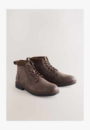 Braune Lederstiefeletten mit abgerundeter Spitze, ausgestattet mit Schnürsenkeln, Metalösendetails, Kordkragen und strukturierter Gummisohle.