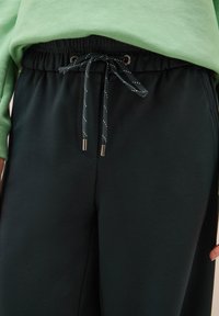 Pantaloni jogger neri con vita elastica e lacci regolabili. Tessuto testurizzato, tasche laterali e dettagli di cucitura discreti.