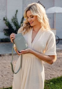 Green leather crossbody bag with a textured finish, zip closure, and adjustable strap. Features a logo embossed on the front.