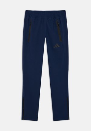Pantalons de sport navy en tissu extensible, avec une ceinture élastique à cordon de serrage, des poches zippées et des zips noirs à la cheville.