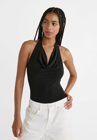 Crni bodysuit s halter-izrezom i drapiranim dekolteom. Napravljen od glatkog materijala. Nosio se s bijelim trapericama visokog struka.