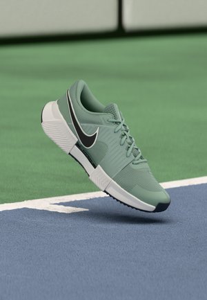 Hele roheline spordijalats valge tallaga ja musta Nike logoga, hõljumas sinisel ja rohelisel väljaspordiväljaku pinnal.