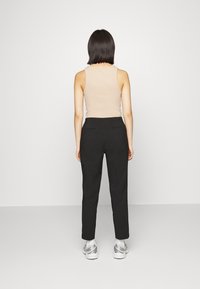 Beige linne tillsammans med svarta skräddarsydda byxor, med hög midja, sidofickor och en slimmad passform. Modellen bär silverfärgade sportskor.