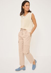 Virkat krämfärgat ärmlöst linne med v-ringning, kombinerat med ljusbeige cargobyxor och blå loafers med låg klack. Minimalistisk design och avslappnad passform.