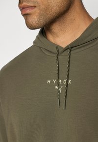 Olivengrønn hettegenser med avslappet passform, med frontlogo, to-tonet snøring og myk tekstur.