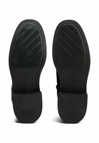 Black shoe soles with diagonal tread patterns and textured heels, embossed with "Tommy Hilfiger" branding.