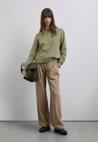 Oliwkowa bluza, beżowe plisowane szerokie spodnie, czarne buty na platformie i mała oliwkowa torebka. Gładkie, casualowe tekstury tkanin.