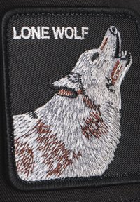 Patch nero con un lupo grigio ricamato che ulula, accentuato da dettagli in pelliccia marrone. Il testo sopra recita "LONE WOLF" in bianco.