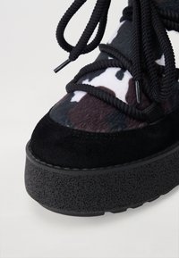 Zapatillas de gamuza negra y tela texturizada con suela de plataforma gruesa. Presenta cordones negros gruesos y un patrón de camuflaje en la sección superior.