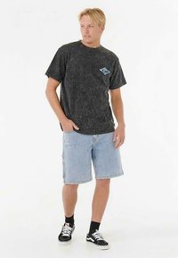 Graues T-Shirt mit Sprenkeln und blauem Logo, kombiniert mit hellblauen Jeansshorts. Trägt schwarze Turnschuhe mit weißen Akzenten und Knöchelsocken.