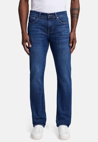 Granatowe dżinsy o prostym kroju nogawki, z zapięciem na guzik, pięcioma kieszeniami i delikatnym wypłowieniem. Połączone z białymi sneakersami.