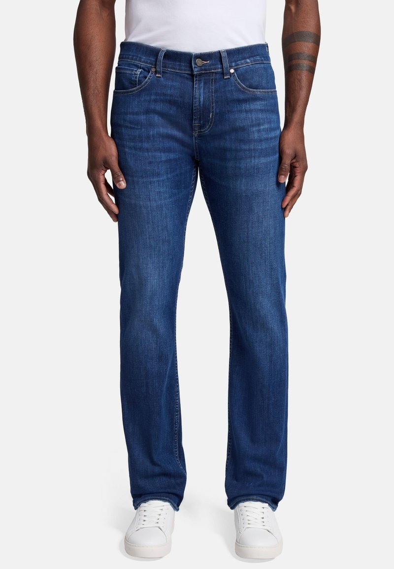 Granatowe dżinsy o prostym kroju nogawki, z zapięciem na guzik, pięcioma kieszeniami i delikatnym wypłowieniem. Połączone z białymi sneakersami.