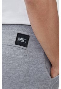 Grey cotton sweatpants with a ribbed waistband and side pockets. Features a black square label with white text on the back.