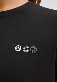 Három fehér ikon középen egy fekete pólón: Lululemon logó kitöltött körben, egy földgömb és Lululemon logó körvonalazott körben.