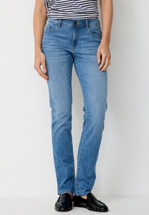 Person wearing light blue straight-leg jeans, black loafers, and a black-and-white striped shirt, standing against a white background.