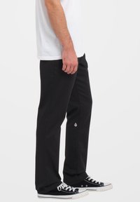 Pantaloni in cotone neri con taglio dritto, caratterizzati da un piccolo logo. Indossati con una maglietta bianca semplice e sneakers nere.