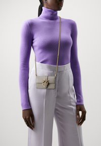 Lilla tettsittende turtleneck genser i kombinasjon med lyse grå bukser. Tilbehøret inkluderer en liten grå crossover-veske med gullkjede og dekorativt hardware.