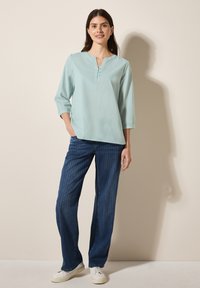 Blusa azzurra chiara con scollo a V e maniche a tre quarti; abbinata a pantaloni larghi a righe blu scuro e sneakers bianche.