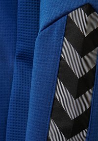 Close-up van blauw stof met zwarte en witte chevronstrepen op een gestructureerd kledingstuk.