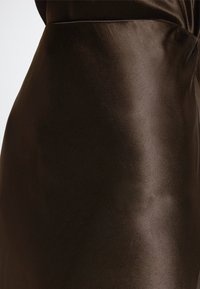 Nærbilde av et skinnende mørkebrunt lærskjørt som fremhever det glatte teksturet og subtile sømdetaljer.