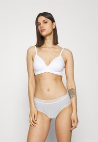 Hvit trådløs BH med en glatt, teksturert overflate og dyp utringning, sammen med hvite bikiniunderdeler med blondeaksenter.