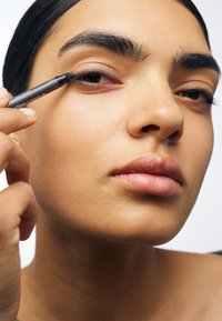 Person applying dark eyeliner to upper eyelid with a makeup pencil, focusing on precise application near the lash line.