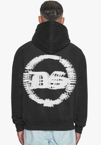 Felpa nera con cappuccio con una grande grafica bianca sulla parte posteriore che presenta le lettere "DS" in un design circolare. Il tessuto sembra morbido.
