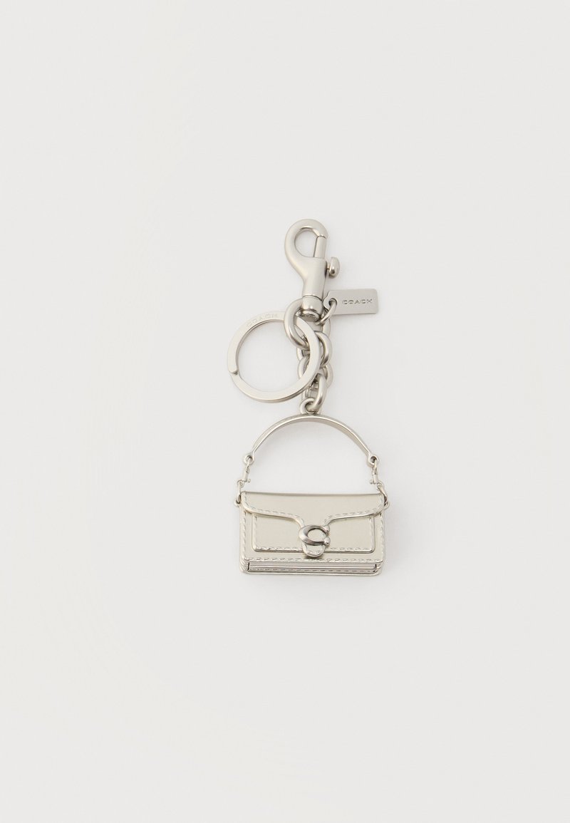 Porte-clés en métal argenté avec un charm en forme de mini-sac à main, un anneau rond et un mousqueton sur fond blanc.